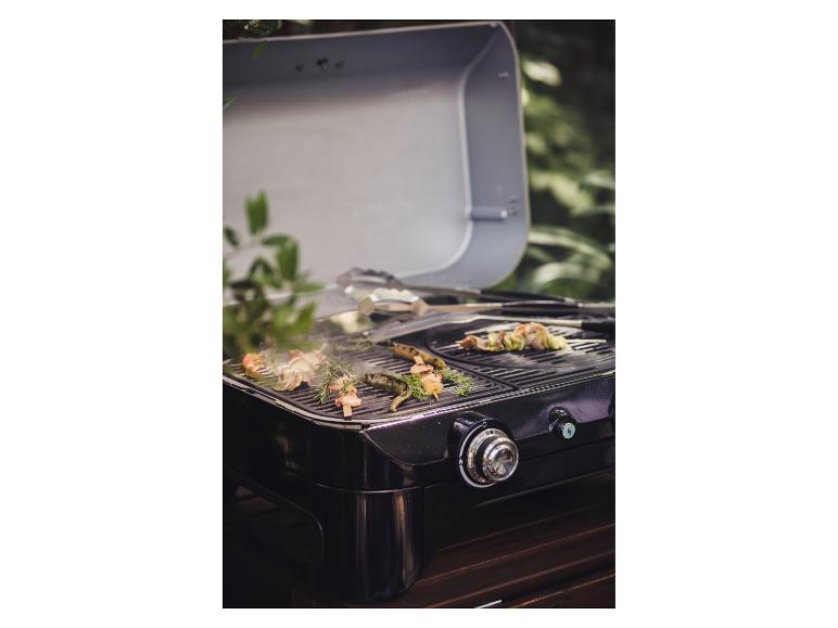 Tragbarer Gasgrill mit Spießen und Gemüse, das auf dem Rost gart.