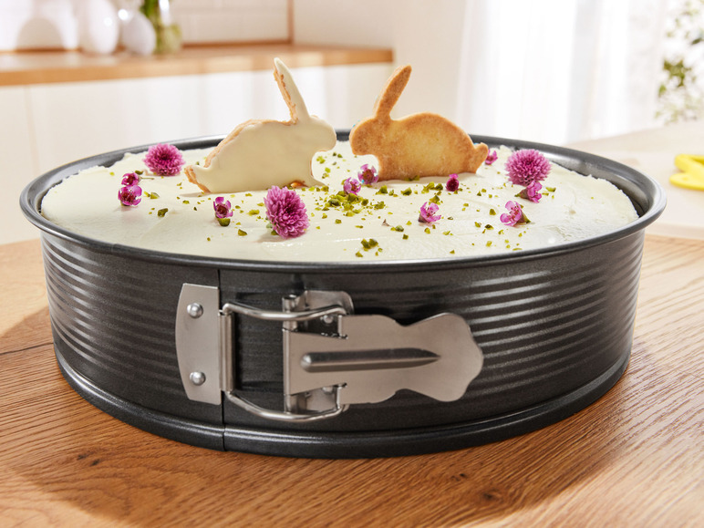 Eine Kuchenform mit einem weißen Kuchen, der mit lila Blumen und Hasenkeksen dekoriert ist