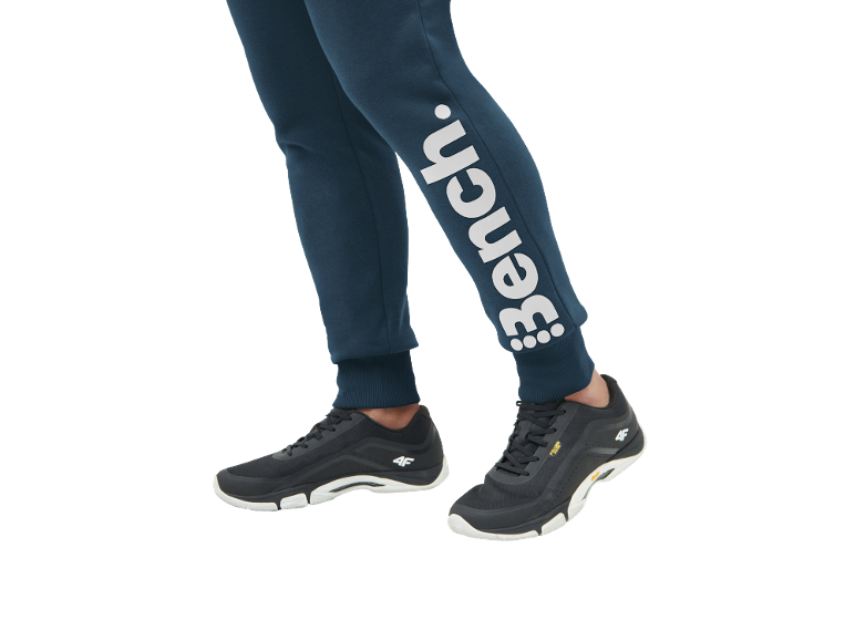 Person trägt dunkelblaue Jogginghose mit weißem Logo und schwarze Sportschuhe.