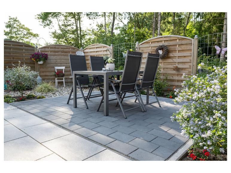 Graue Gartenmöbel auf einer gepflasterten Terrasse, umgeben von Grün und einem Holzzaun.