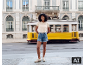 Frau in beigem Pointelle-T-Shirt und Denim-Shorts vor einer gelben Straßenbahn.