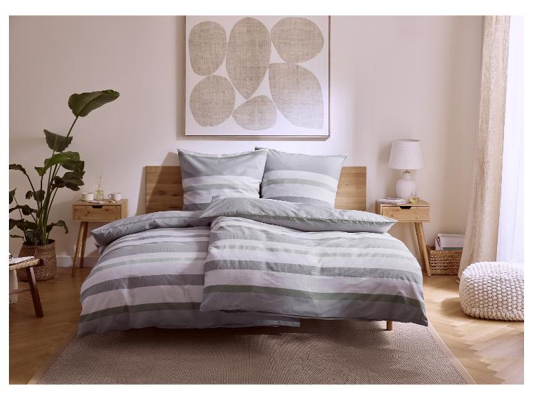 Schlafzimmer mit grau-weiß gestreifter Bettwäsche, Holzdetails und einer großen Pflanze.