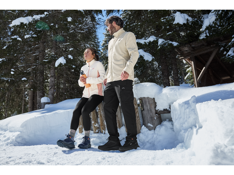 Mann und Frau in Winterkleidung und Schuhen in einem verschneiten Wald.
