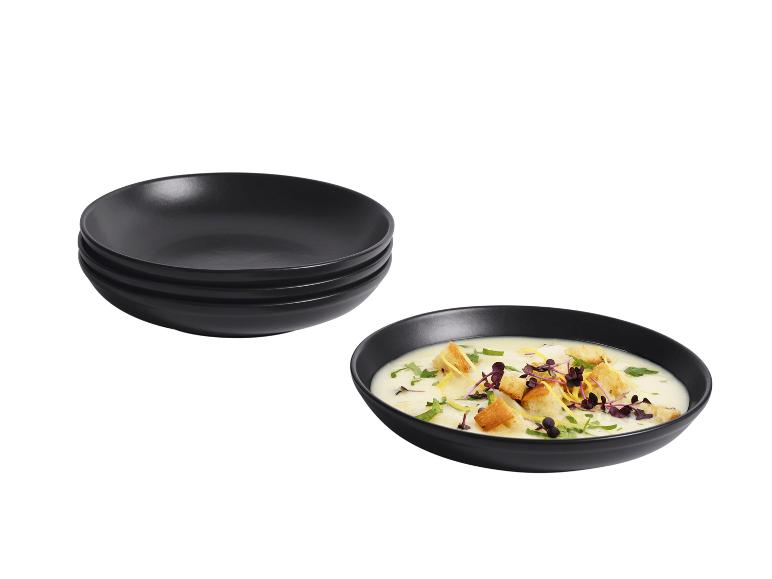 Gestapelte schwarze Suppenteller und eine Schüssel Suppe mit Croutons und Kräutern.