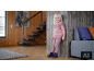Kleinkind in rosa Pullover und Leggings, das an einer Holzwand lehnt.