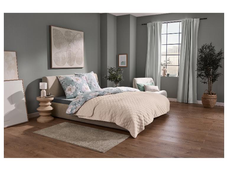 Schlafzimmer mit Bett, floralem Bettbezug, gesteppter Tagesdecke und Beistelltisch.