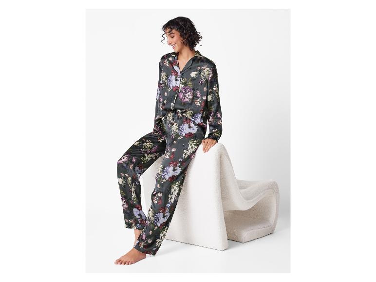 Lächelnde Frau in Satin-Pyjama mit Blumenmuster, sitzt auf einem weißen Stuhl.