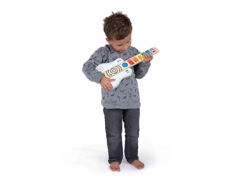 Ein kleiner Junge spielt eine weiße und hölzerne Spielzeuggitarre mit bunten Knöpfen.