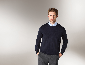 Mann in dunkelblauem Pullover, hellblauem Hemd und grauer Hose.