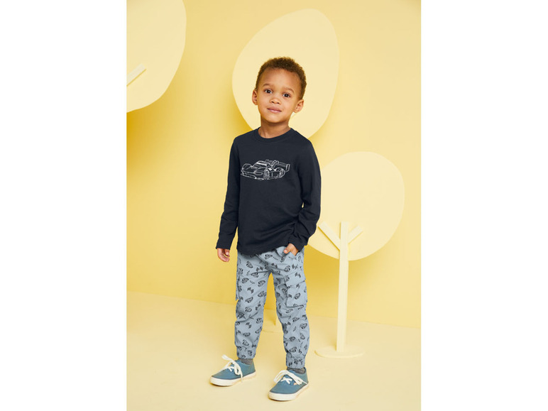 Junge trägt ein schwarzes Langarmshirt mit Rennautodruck und blaue Hose mit Autodruck.