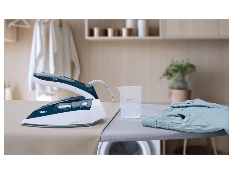 Dampfbügeleisen mit Messbecher und Jeans auf einem Bügelbrett im Waschraum.