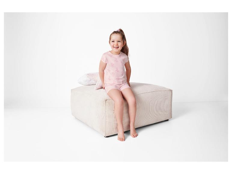 Rosa Pyjama mit Muster, Kind sitzt auf einem beigen Hocker.