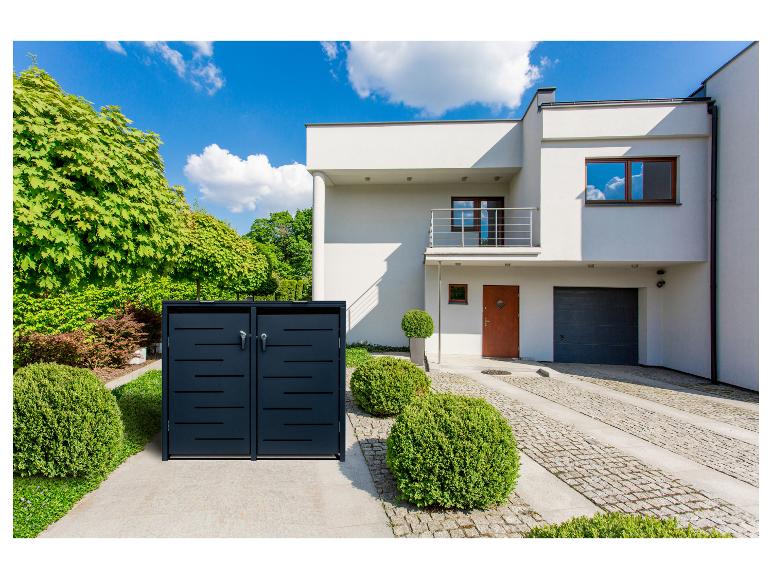 Dunkelgraue Mülltonnenbox vor einem modernen weißen Haus mit grünen Büschen und Bäumen.