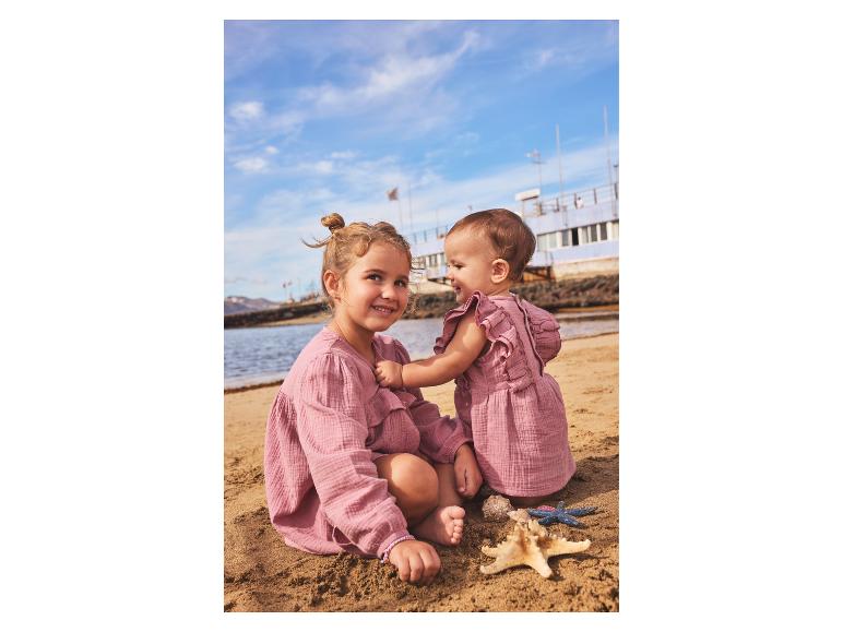 Zwei Kinder in rosa Sommerkleidern spielen am Strand mit Seesternen.