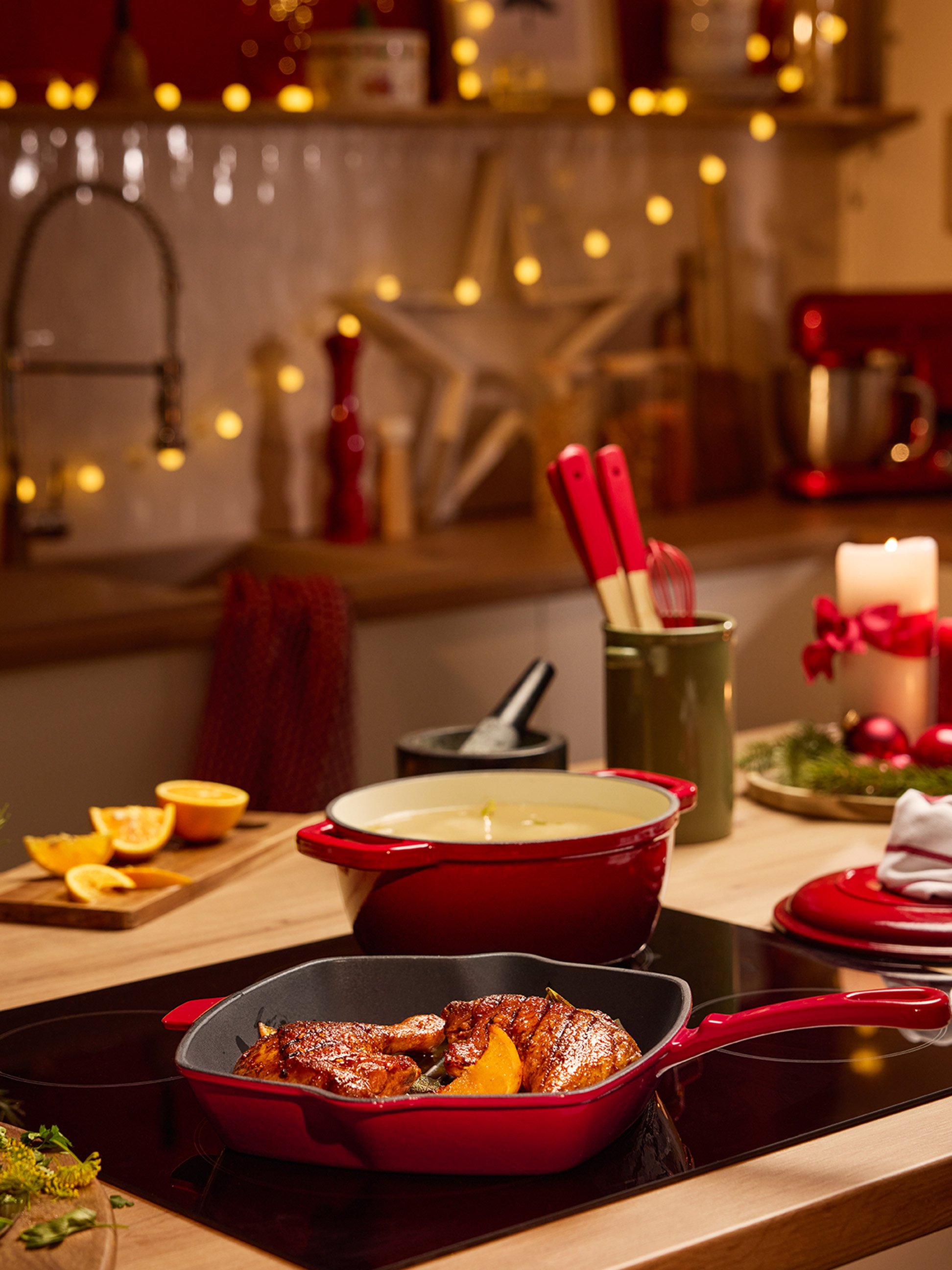 Rote Töpfe und Pfannen mit Essen auf einem Kochfeld in einer weihnachtlich dekorierten Küche.