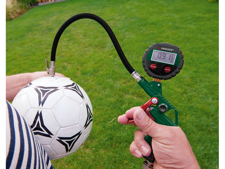 Digitales Reifendruckmessgerät pumpt einen Fußball auf grünem Rasen auf.