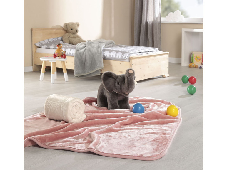 Eine rosa Decke mit einer weißen Decke und einem Elefanten-Spielzeug in einem Kinderzimmer.