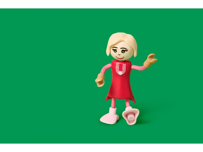 Spielzeugmädchen in rotem Kleid mit blonden Haaren auf grünem Hintergrund.
