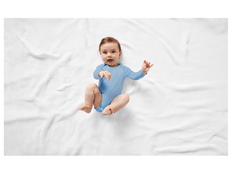 Lächelndes Baby auf einer weißen Decke in einem blauen Body.