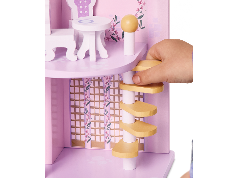 Kinderhand spielt mit einem rosa Holzpuppenhaus, mit Möbeln und Wendeltreppe.