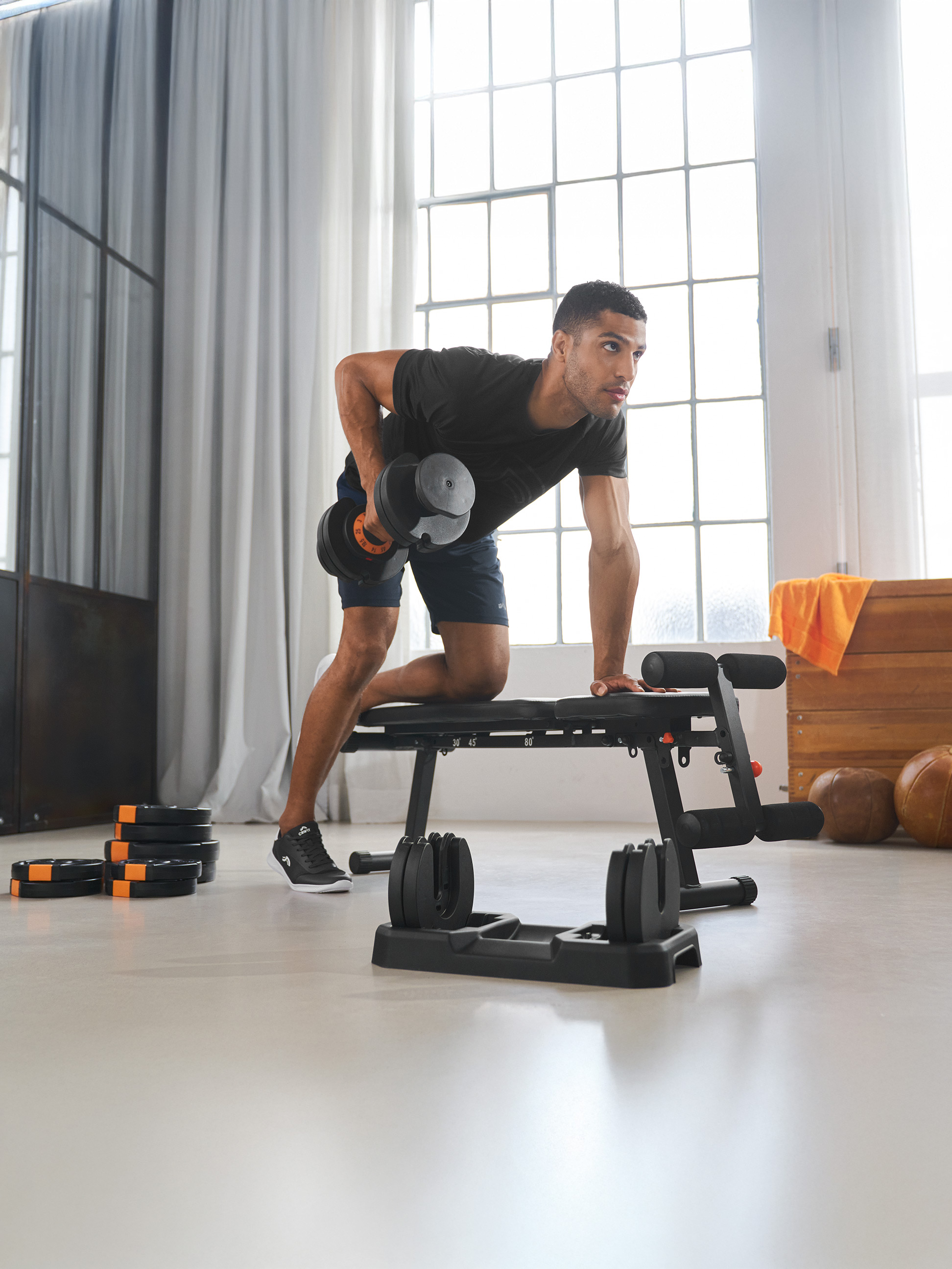 Mann trainiert mit verstellbarer Hantel und Hantelbank in einem hellen Raum.