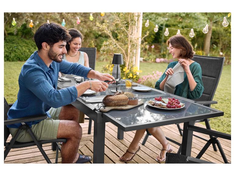 Drei Personen sitzen an einem Gartentisch mit grauer Platte, essen Brot und Trauben.