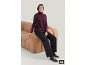 Frau in lila Strickpullunder, schwarzer Hose und Stiefeletten sitzt auf einem Sofa