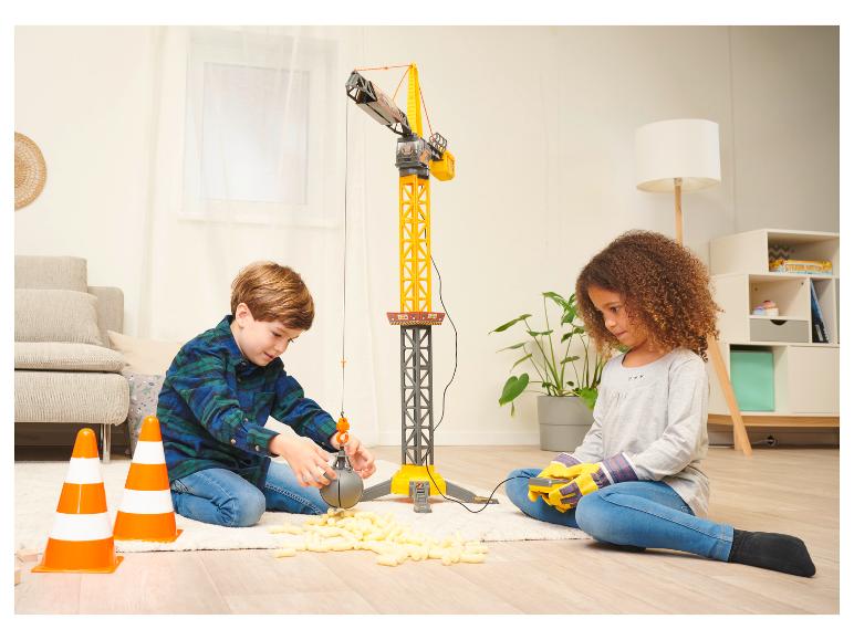 Zwei Kinder spielen mit einem großen Spielzeugkran und Verpackungschips auf einem Teppich.