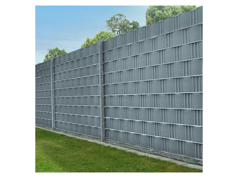 Ein grauer Zaun mit einem gewebten Muster, sichtbar vor einem Hintergrund aus grünem Gras.