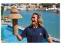 Lächelnde Person hält eine korkene Pilzlampe an einem Pool mit See und Gebäuden im Hintergrund.