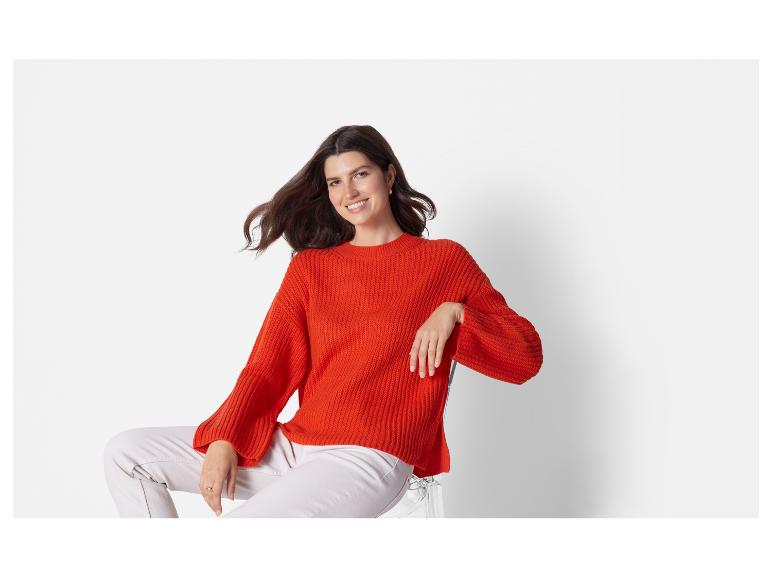 Eine Frau trägt einen orangen Pullover und weiße Hosen.