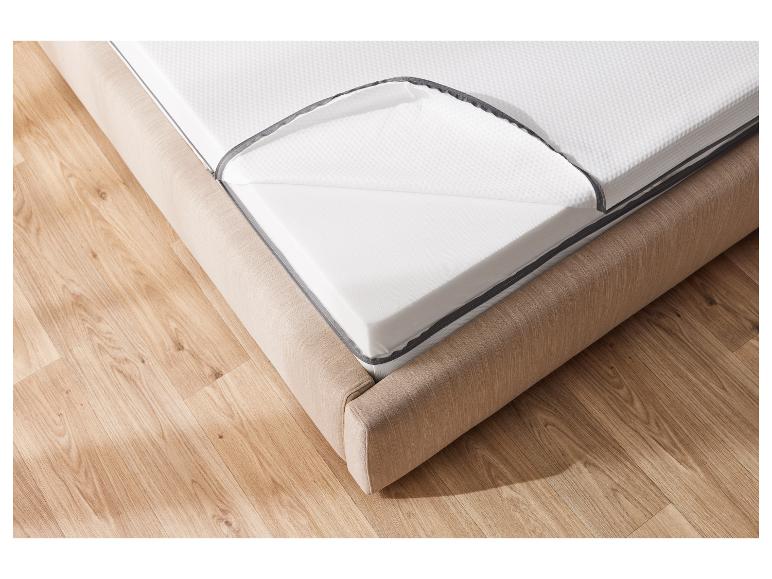 Schaumstoffmatratze mit Reißverschlussbezug auf beigem Bett, auf Holzboden.