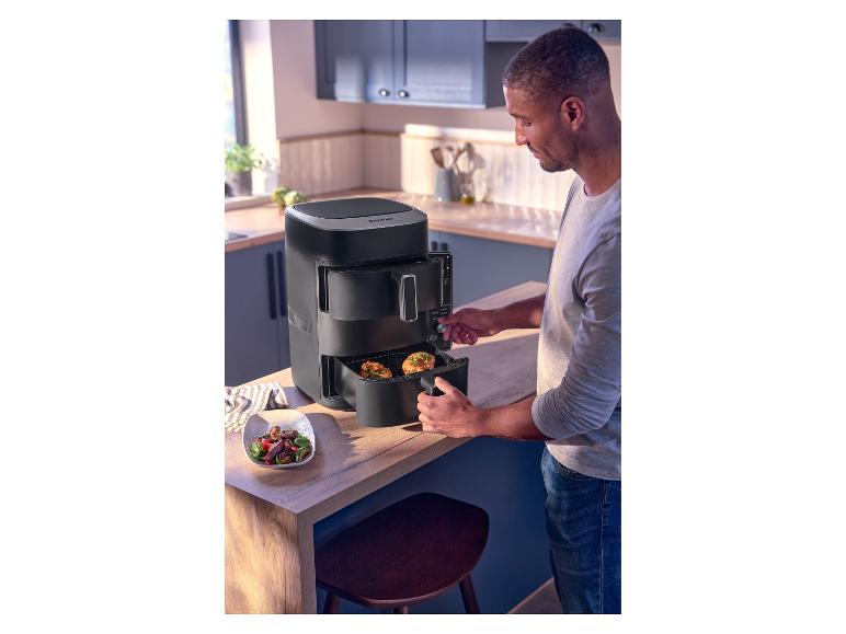 Mann benutzt eine schwarze Heißluftfritteuse in der Küche, daneben eine Schüssel Salat.