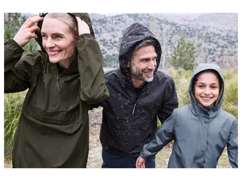 Eine glückliche Familie trägt Regenjacken bei einem Spaziergang im Regen.