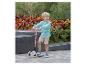 Blonder Junge in kariertem Hemd und beigen Shorts auf einem rosa Dreirad-Roller.
