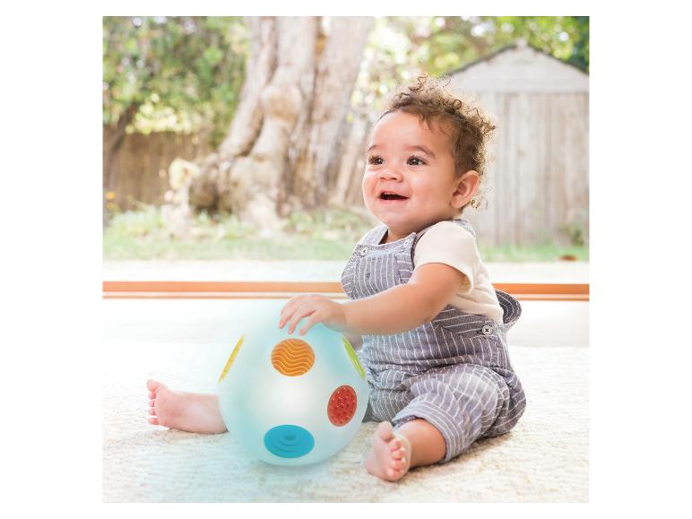Lächelndes Baby im gestreiften Strampler, spielt mit einem bunten Sensorikball.