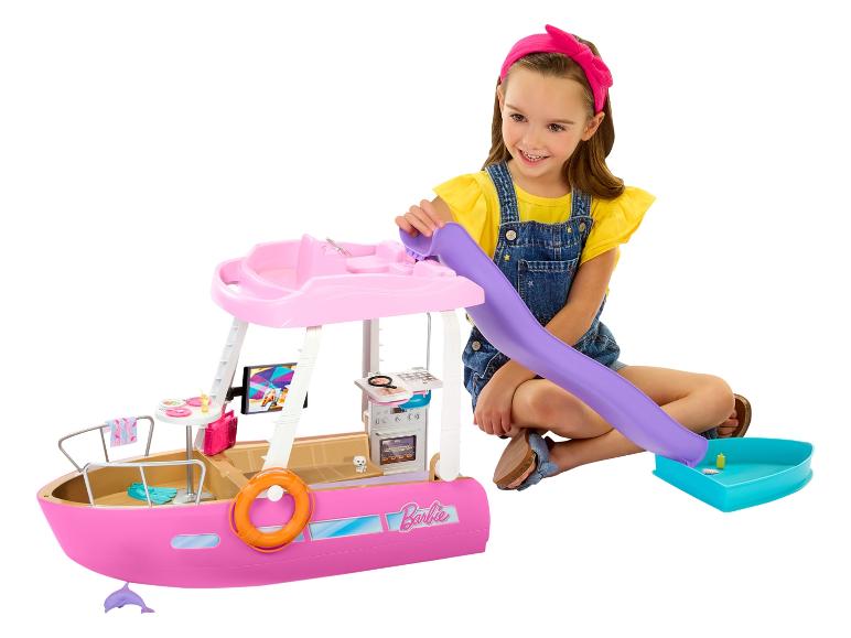 Ein lächelndes Mädchen spielt mit einem pinken Barbie-Spielzeugboot, mit Rutsche und Zubehör.