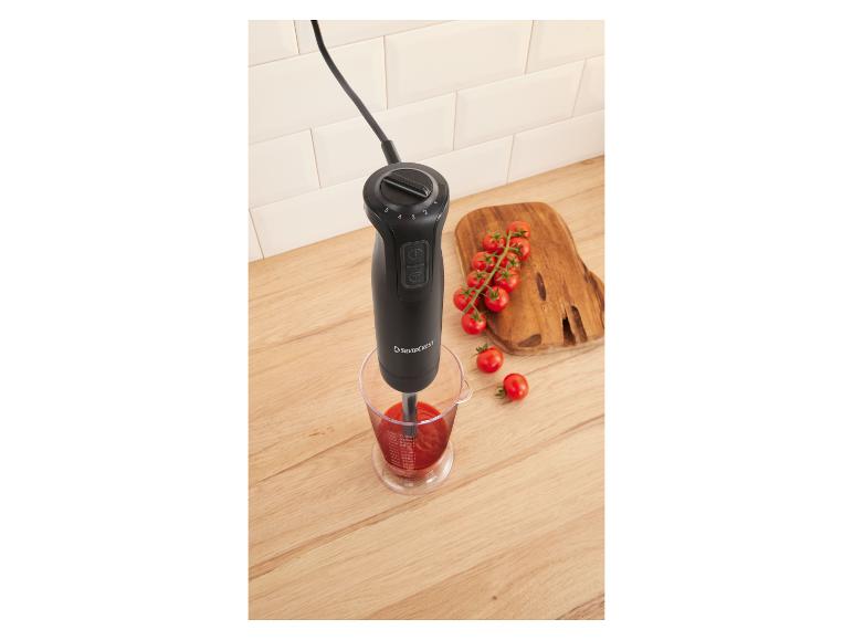 Stabmixer in einem Messbecher mit Tomatensauce, Kirschtomaten auf einem Holzbrett