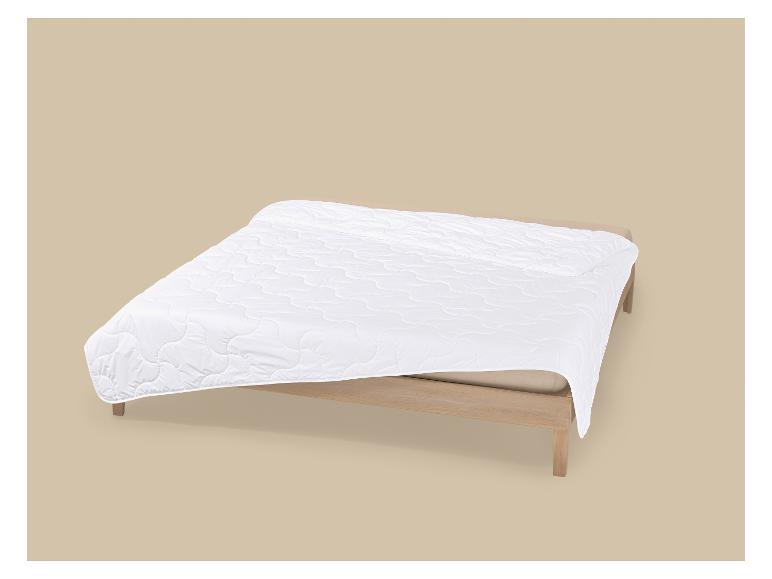 Weiße Steppdecke auf einem Holzbett vor beigem Hintergrund