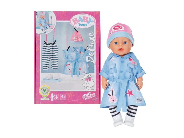 BABY born Deluxe Puppe im blauen Kleid mit Hasen und rosa Mütze, neben der Verpackung.