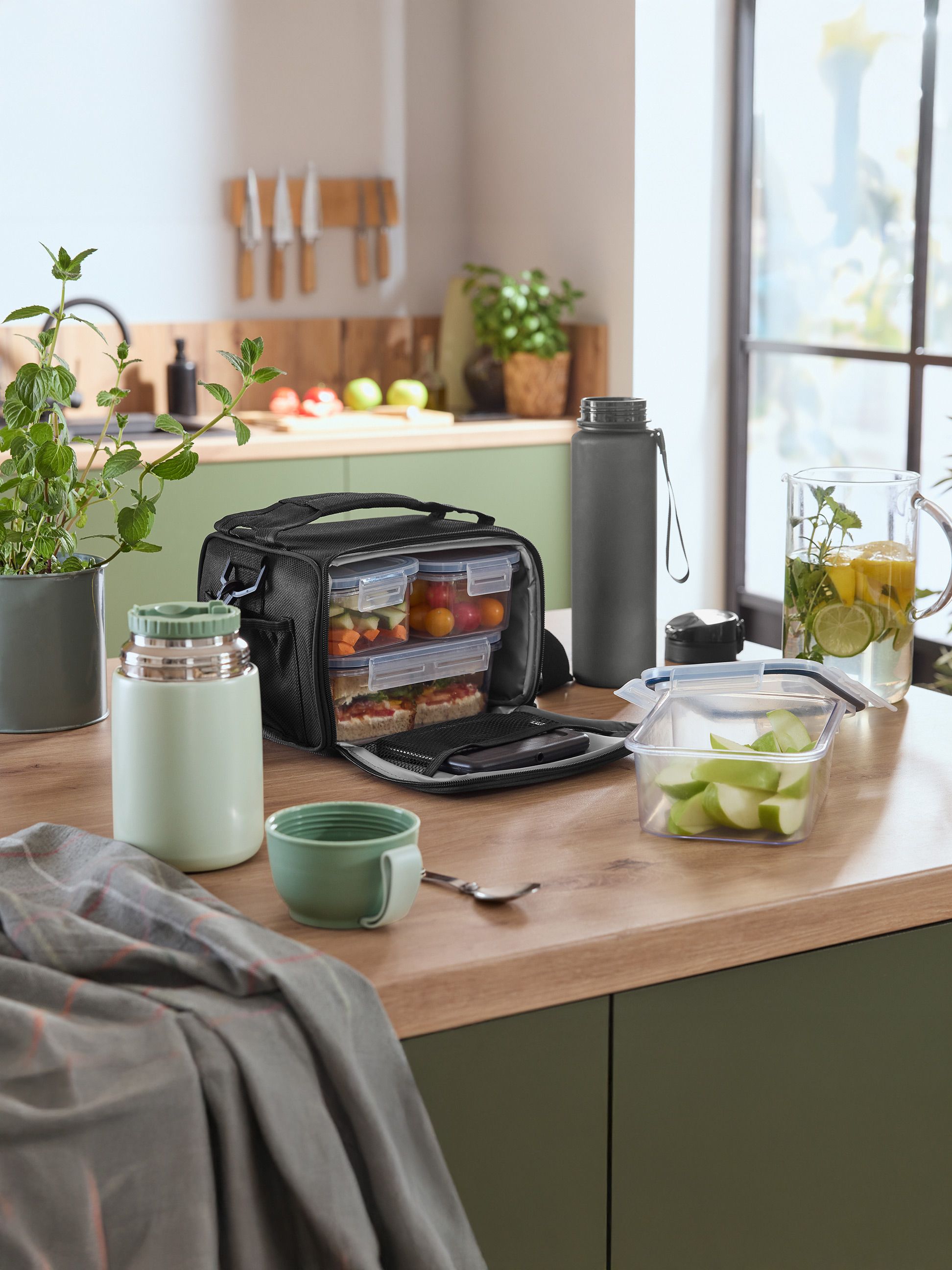 Kühltasche mit Essensbehältern, Thermoskanne und Wasserflasche auf einer Küchenarbeitsplatte.
