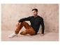 Ein Mann trägt einen schwarzen Pullover, eine braune Cordhose und weiße Sneaker.