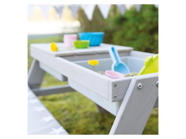 Sandkastentisch mit buntem Spielzeug und Sand in einem Garten.