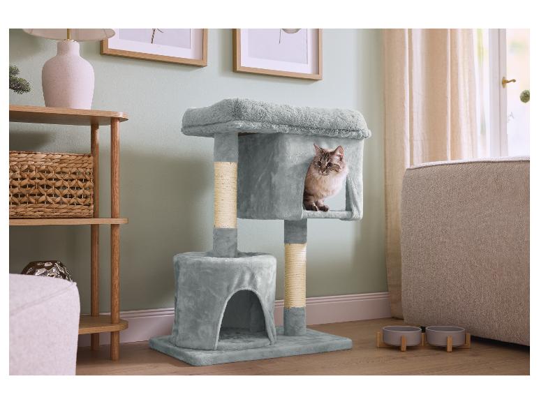 Eine Katze in einem grauen Katzenbaum, neben einem Holzregal und Haustiernäpfen.