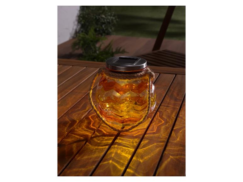 Eine solarbetriebene Glaslaterne mit Zickzackmuster auf einem Holztisch.