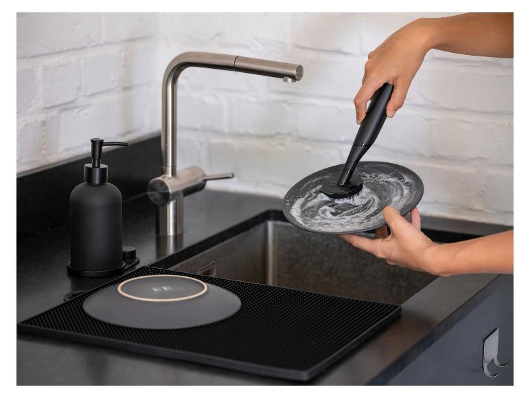 Eine Frau spült einen Teller mit einem elektrischen Geschirrspüler in der Küche.