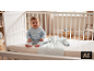 Glückliches Baby im blauen Schlafanzug mit Eisbärmotiv, sitzend in einem weißen Kinderbett.