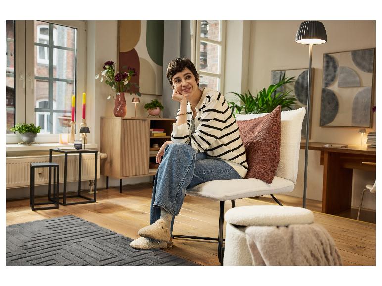 Lächelnde Frau in einem gemütlichen Sessel, mit modernen Möbeln und Wohnaccessoires.