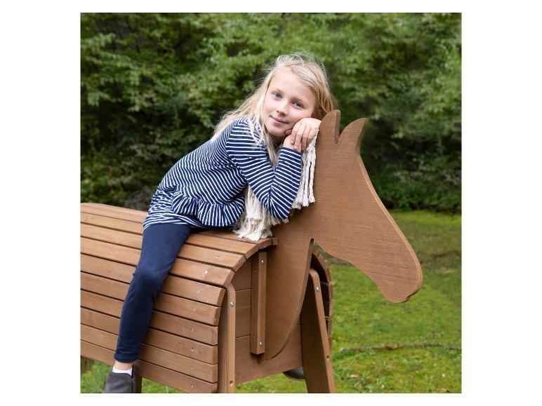 Blondes Mädchen sitzt auf einem hölzernen Spielpferd im Freien.