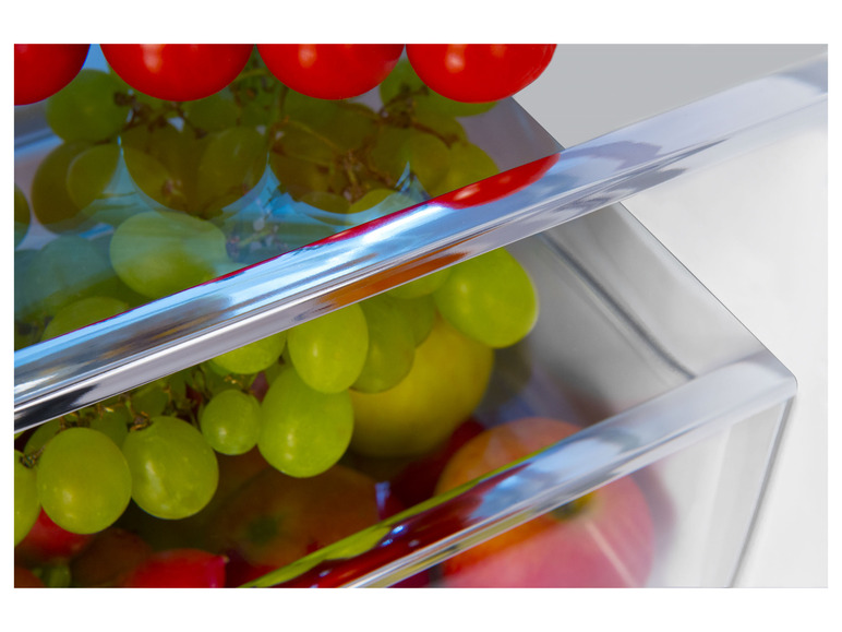 Grüne Trauben und rote Tomaten in einer transparenten Kühlschublade.